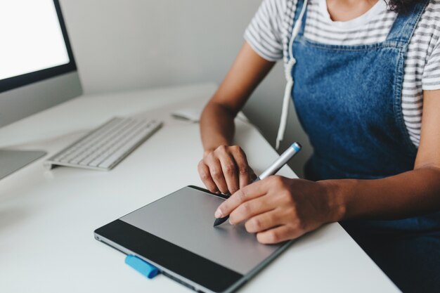 Photo en gros plan d'une fille à la peau brun clair travaillant avec un nouvel appareil alors qu'il était assis au bureau