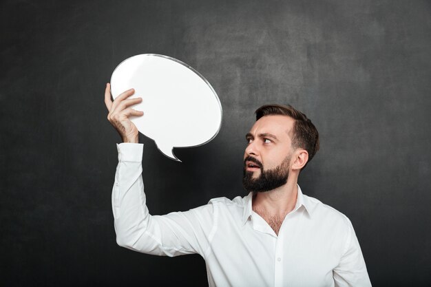 La photo en gros plan d'un homme séduisant tenant un message vide ballon et regardant l'annonce sur un mur gris foncé copie espace