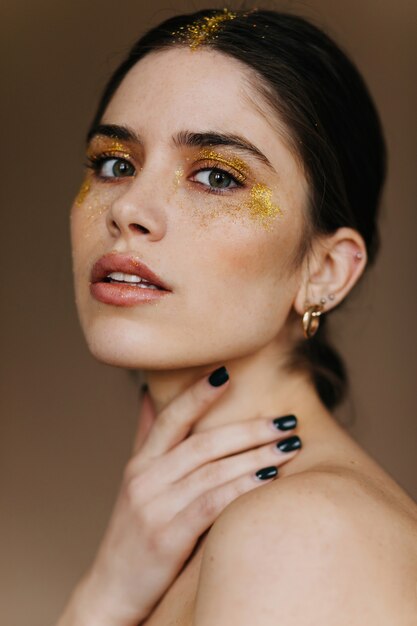 Photo en gros plan d'une jeune femme curieuse en bijoux dorés. femme brune glamour en boucles d'oreilles.