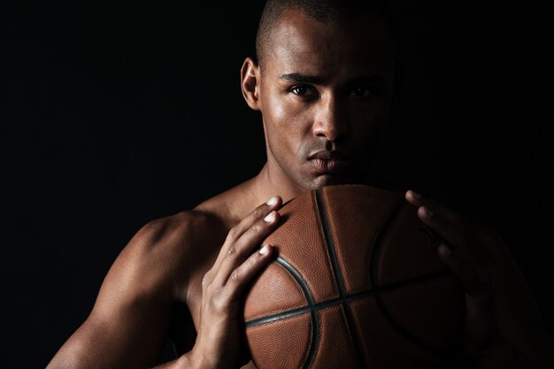 Photo en gros plan d'un joueur de basket-ball afro-américain sérieux tenant le ballon à deux mains