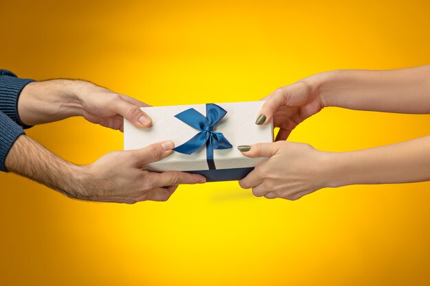 Photo gros plan des mains de l'homme et de la femme avec boîte-cadeau sur fond jaune