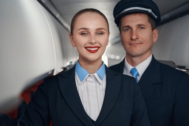 Photo en gros plan d'un pilote d'avion masculin et d'une hôtesse de l'air regardant la caméra tout en souriant dans la cabine passagers