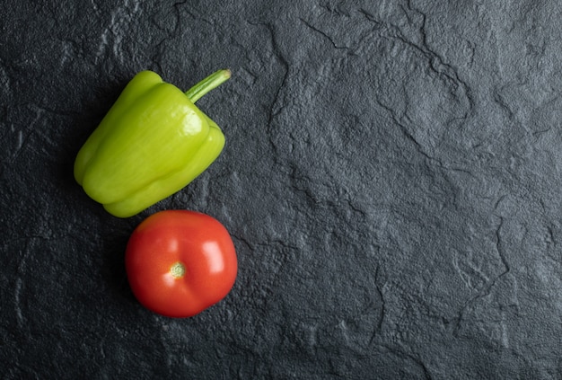 La photo en gros plan de la tomate et du poivre sur fond noir