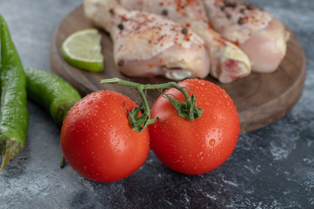 La photo en gros plan de tomates et poivrons biologiques frais avec des cuisses de poulet cru.