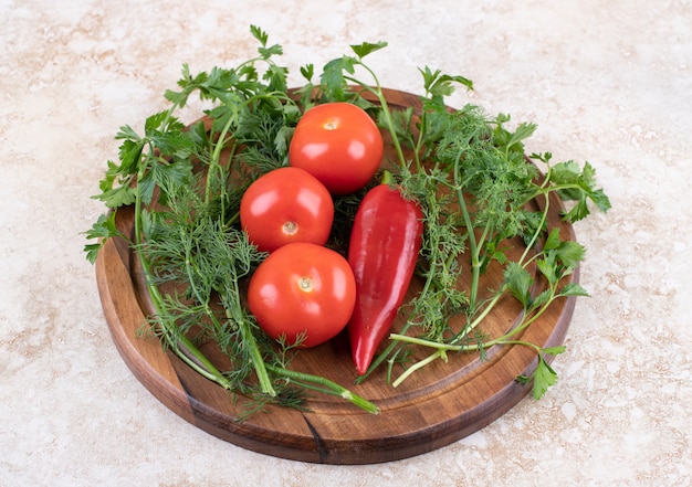 La photo en gros plan de tomates et de poivrons avec des verts sur planche de bois.