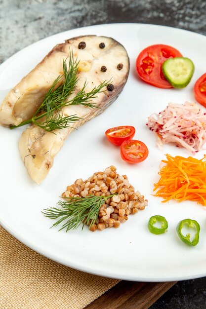 Photo haute résolution de farine de sarrasin de poisson bouilli servi avec des légumes verts sur une assiette blanche sur une serviette nue sur une planche à découper en bois sur une surface de glace