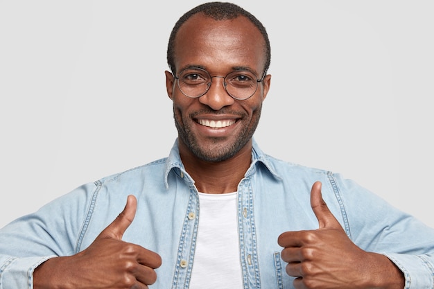 Photo gratuite photo de l'heureux homme adulte à la peau sombre avec chaume soulève les pouces et sourit largement