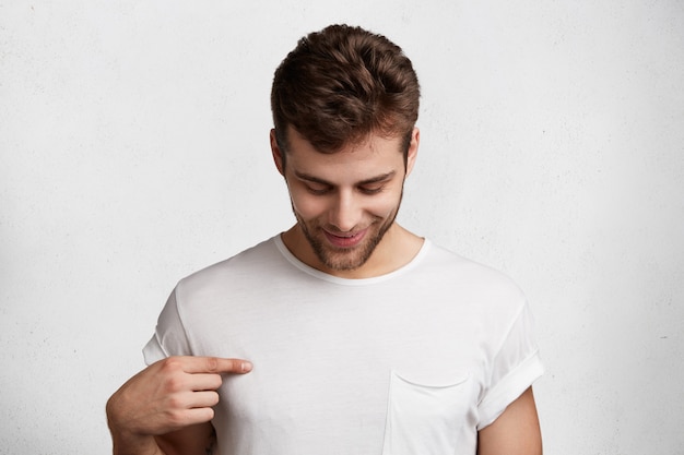 Photo d'un homme brun regarde vers le bas, indique un t-shirt blanc, étant de bonne humeur