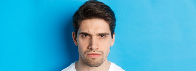 Photo gratuite photo d'un homme en colère fronçant les sourcils qui a l'air déçu et gêné debout sur fond bleu