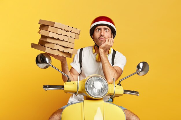 Photo d'homme livreur avec casque de conduite scooter jaune tout en tenant des boîtes de pizza