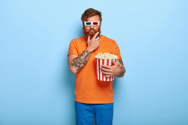 Photo d'un homme rousse barbu sérieux mange du pop-corn