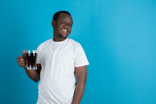 Photo d'un homme en t-shirt blanc tenant une tasse de vin en verre contre un mur bleu