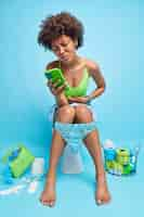 Photo gratuite photo d'intérieur d'une femme afro-américaine souffrant de crampes abdominales a la constipation recherche sur internet quel médicament prendre tient des poses de téléphone portable dans les toilettes sur la cuvette des toilettes