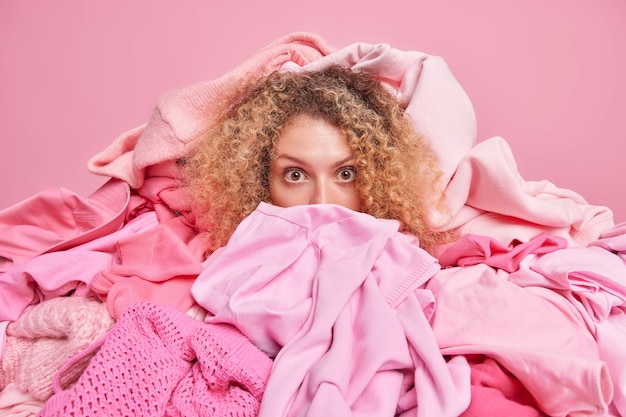 Photo gratuite une photo d'intérieur d'une femme choquée entourée de vêtements roses aide les gens à faire des dons de vêtements à un travail caritatif qui choisit une tenue pour une utilisation ou un recyclage secondaire.