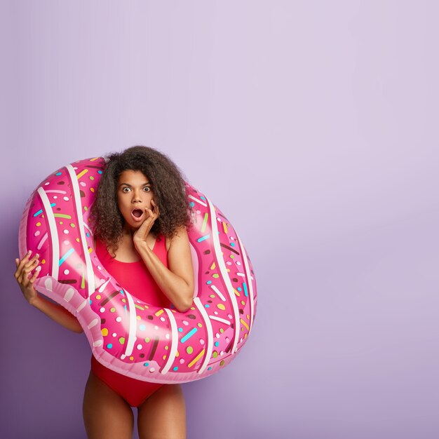 Photo intérieure d'une femme surprise aux cheveux afro, pose avec un anneau gonflé