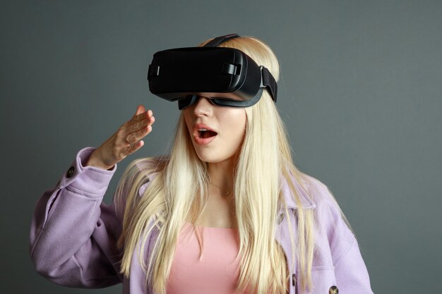 Photo de jeune blonde choquée portant des lunettes VR sur fond gris