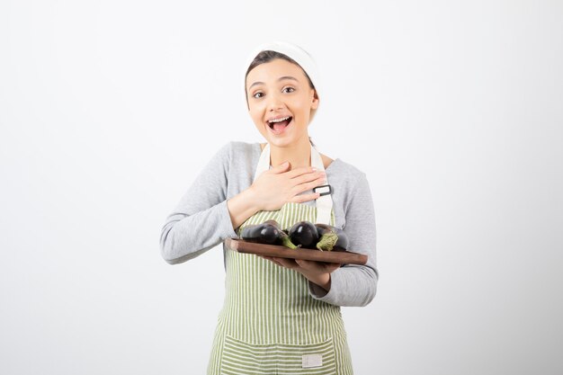 Photo d'une jeune cuisinière tenant une assiette d'aubergines et riant