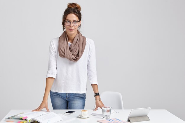 Photo d'un jeune enseignant en tenue élégante, se prépare pour un séminaire ou une leçon, étudie différentes sources littéraires, boit du latte, utilise une tablette pour rechercher des informations sur Internet, isolé sur un mur blanc