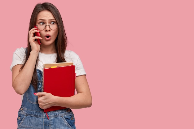 La photo d'une jeune femme asiatique surprise a une expression perplexe, parle par téléphone portable, discute de nouvelles étonnantes