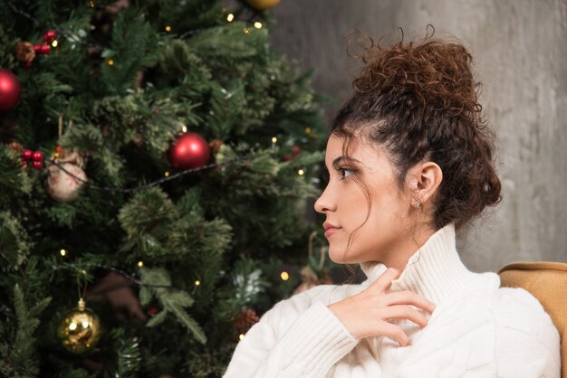 Photo de jeune femme assise dans une chaise confortable près de l'arbre de Noël