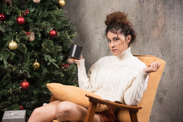 Photo de jeune femme assise dans une chaise confortable avec une tasse de boisson