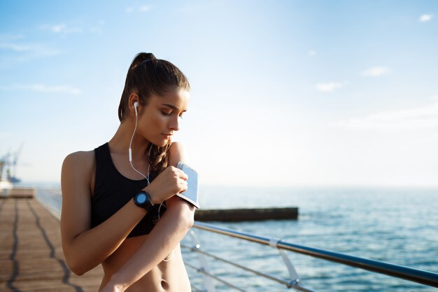 Photo de jeune femme fitness écouter de la musique avec la côte de la mer sur le mur