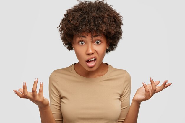 Photo d'une jeune femme hésitante confuse a une coiffure afro bouclée, hausse les épaules