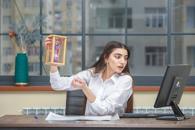 Photo de jeune femme tenant un sablier et regardant le pc