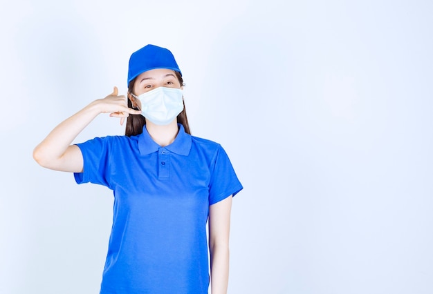 Photo d'une jeune femme en uniforme portant un masque médical et faisant un geste d'appel téléphonique.