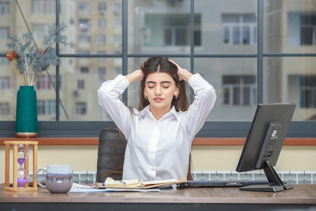 Photo de jeune fille assise au bureau et étirant ses cheveux Photo de haute qualité