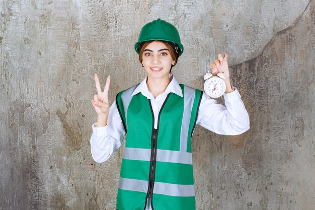 Photo de jeune fille en gilet vert et casque avec réveil montrant le signe de la victoire