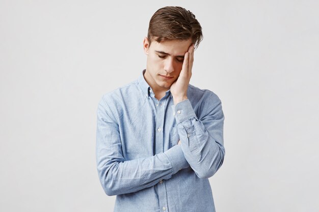 Photo d'un jeune homme épuisé en chemise décontractée bleue.