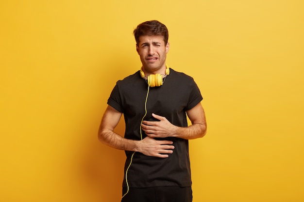 Photo gratuite photo d'un jeune homme européen bouleversé souffre de maux d'estomac, garde les deux mains sur le ventre