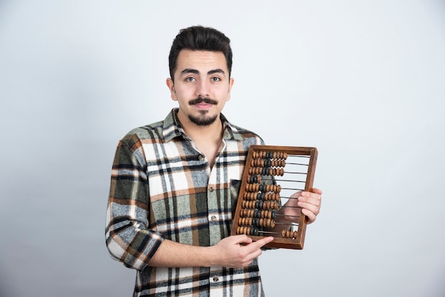 Photo gratuite photo d'un jeune homme avec des perles de comptage en bois debout sur un mur blanc.