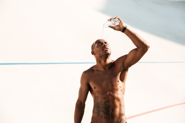 Photo de jeune homme sportif africain versant de l'eau sur la tête