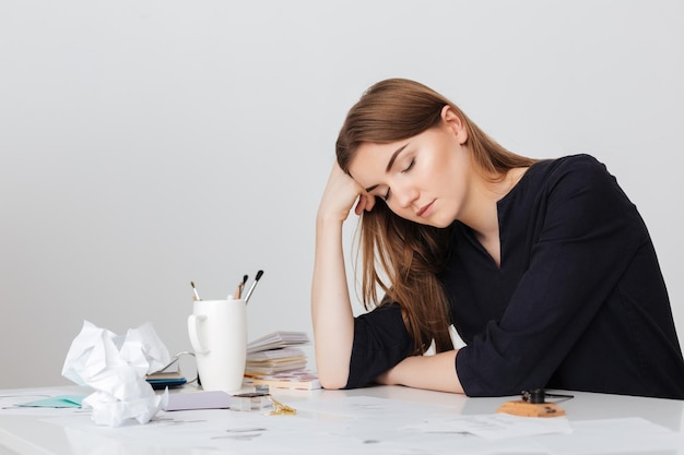 Photo de jolie dame assise au bureau blanc et dormant tout en se penchant la tête sur sa main isolée