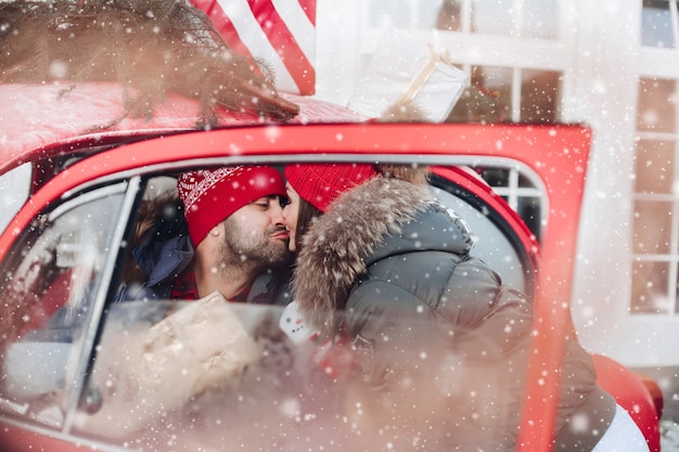 Photo De Jolie Femme De Race Blanche Dans Des Vêtements Chauds Porte Des Boîtes Avec Des Cadeaux De Noël Dans Une Voiture à Son Petit Ami Et L'embrasse