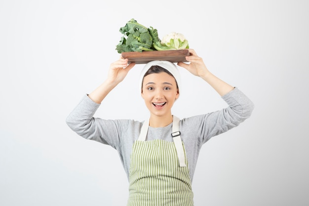 Photo d'une jolie femme souriante tenant une assiette en bois de choux-fleurs au-dessus