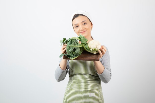 Photo d'une jolie femme souriante tenant une assiette en bois de choux-fleurs