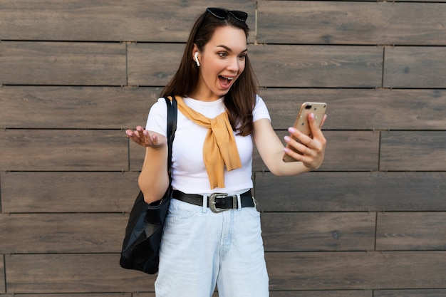 Photo d'une jolie jeune femme surprise choquée portant des vêtements décontractés, debout dans la rue, parlant au téléphone portable en regardant un smartphone