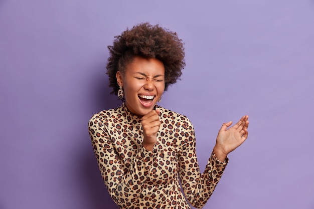 Photo gratuite photo de joyeuse femme afro-américaine tient la main près de la bouche comme microphone, chante des chansons au karaoké, être de bonne humeur, porte des vêtements à imprimé léopard