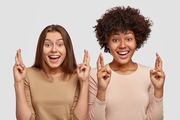 Photo de joyeuses femmes métisses gardent les doigts croisés