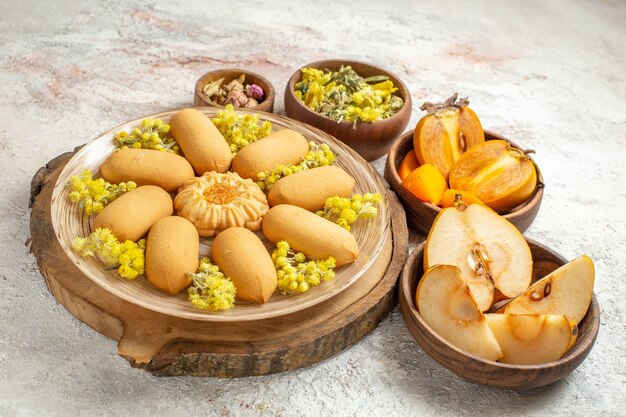 Photo latérale d'une assiette de biscuits sur un plateau en bois et de différentes fleurs et fruits secs