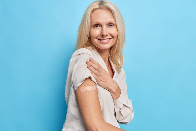 Une photo latérale d'une femme blonde de quarante ans approuve la campagne de vaccination et reçoit l'inoculation du virus covid 19 se sent protégée isolée sur le mur bleu