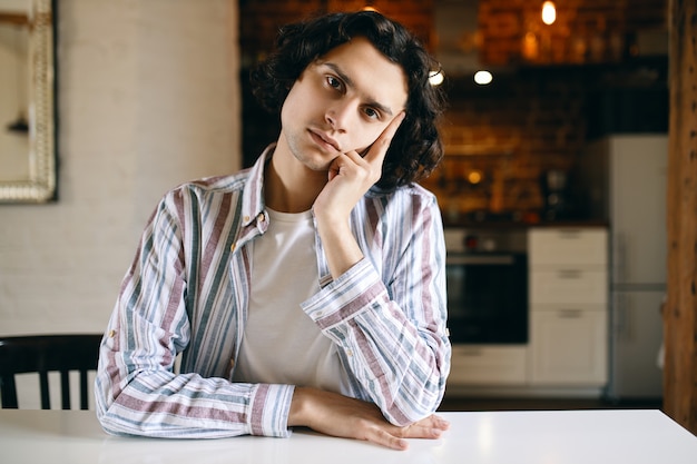 Photo d'un mec mignon dans des vêtements décontractés ayant une expression faciale ennuyée, être désintéressé, assis à table