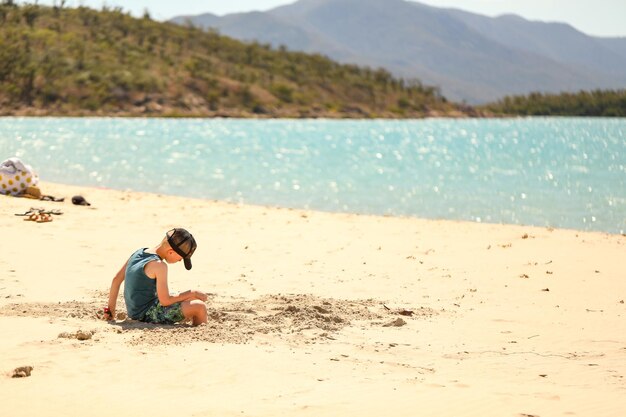 Photo de mise au point peu profonde d'un petit garçon avec une casquette se relaxant sur une plage de sable