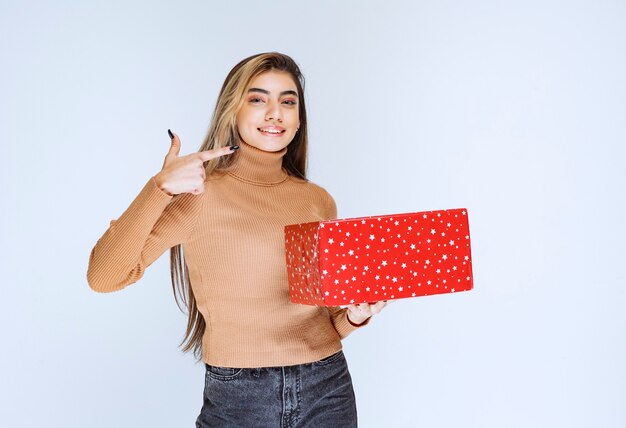 Photo d'un modèle de femme séduisante tenant un cadeau rouge et pointant vers l'extérieur.
