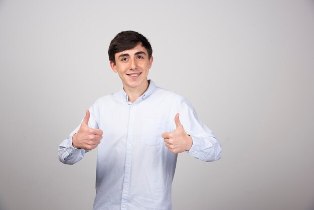 Photo d'un modèle d'homme positif debout et montrant les pouces vers le haut