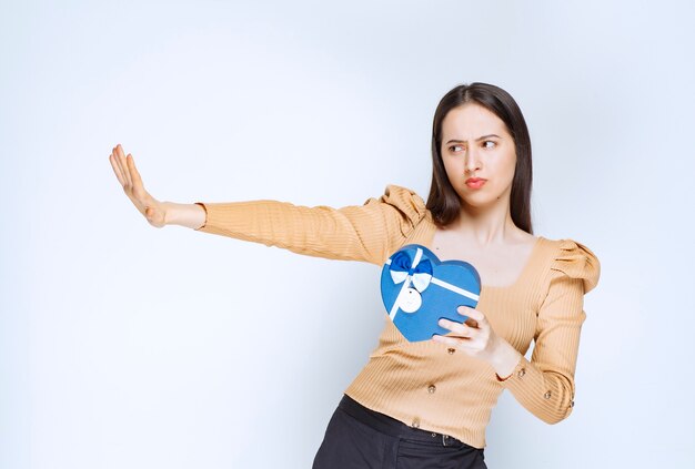 Photo d'un modèle de jeune femme tenant une boîte-cadeau en forme de coeur contre un mur blanc.