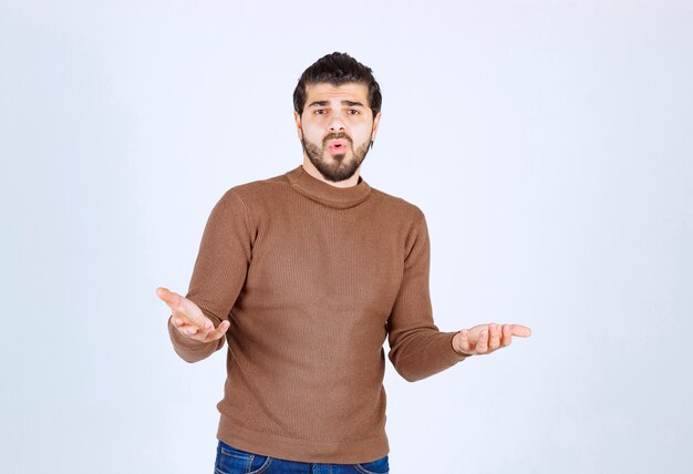 Photo d'un modèle de jeune homme beau debout et posant sur un mur blanc.